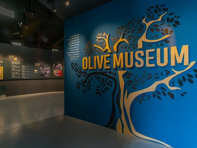 Blue wall with wooden letters reading 'OLIVE MUSEUM' inside.