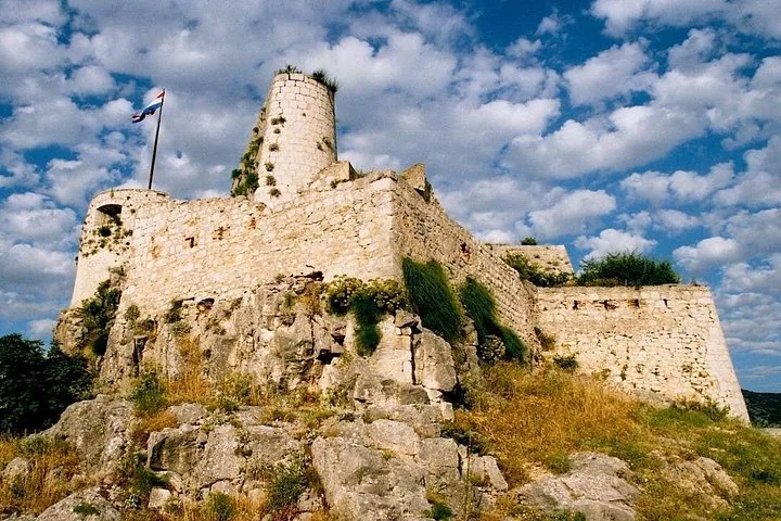 Muros de piedra y torre de vigilancia de la Fortaleza de Klis bajo un cielo nublado.