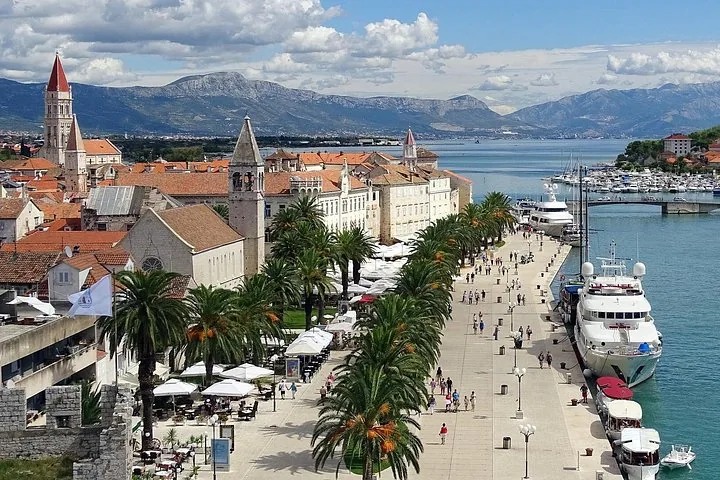 Vista panorámica del paseo marítimo de Trogir, palmeras y yates atracados.
