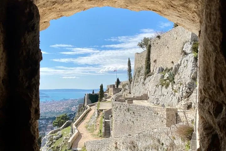 Muros de piedra y caminos de la Fortaleza de Klis enmarcados por un arco.