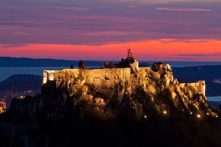 Illuminated Klis Fortress on a rocky hill at dusk.