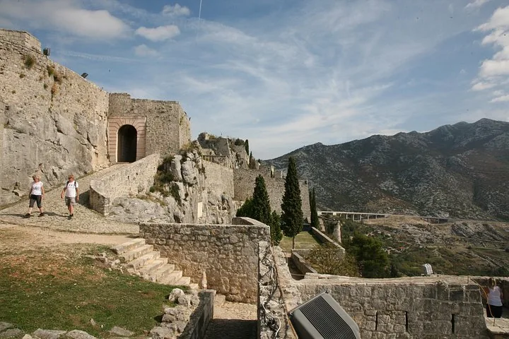 Two people walking along the stone ramparts of Klis Fortress.